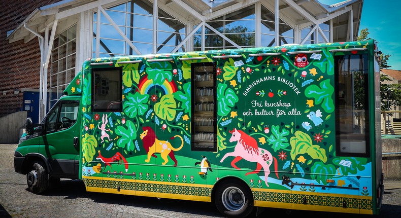 Simrishamns biblioteks bokbuss, som är grön och rik på djur- och växtillustrationer står parkerad framför Simrishamns bibliotek.