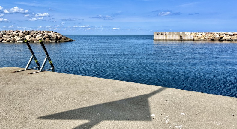 Blå himmel och blått hav möts mellan två vågbrytare en vacker sommardag i Baskemöllas hamn.