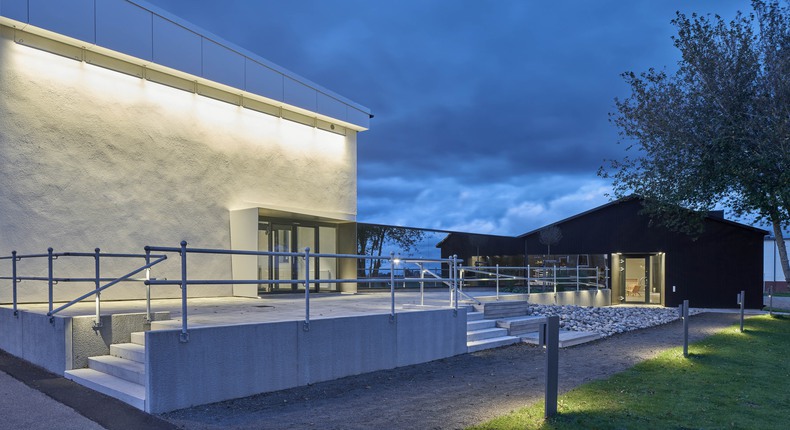 Bild av en upplyst del av Gärsnäs möblers byggnation. Vit fasad med glaspartier. Trappa i betong med räcke. Gärsnäs möbler, vinnare av arkitekturpriset 2019.