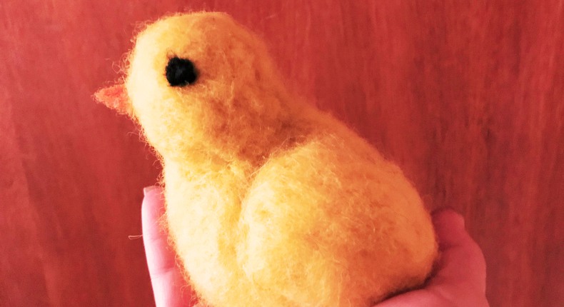 En gul tovad kyckling sitter i en kupad hand.