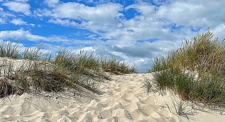Sanddynor i solen mot en blå himmel med via moln.