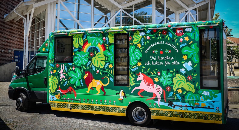 Simrishamns biblioteks bokbuss, som är grön och rik på djur- och växtillustrationer står parkerad framför Simrishamns bibliotek.