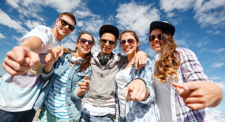 Flera tonåringar  i solglasögon håller om varandra och pekar in mot kameran