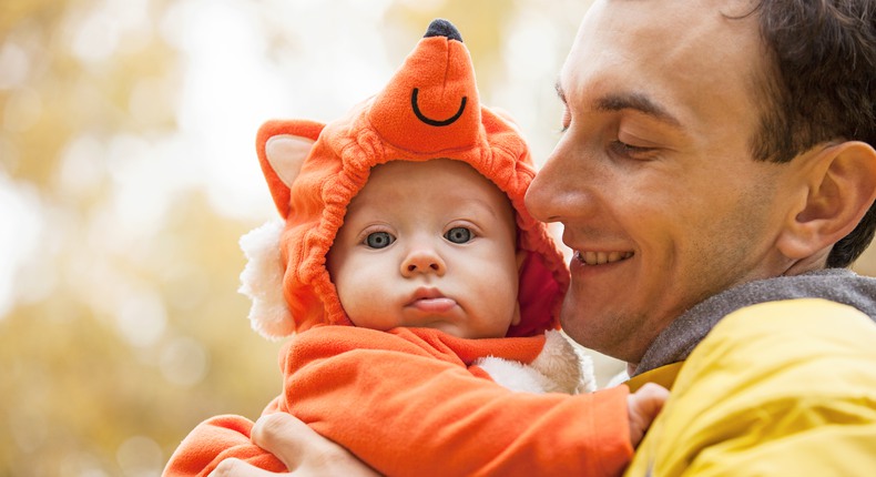 En pappa håller en bebis i famnen. Bebisen är utklädd till räv. 