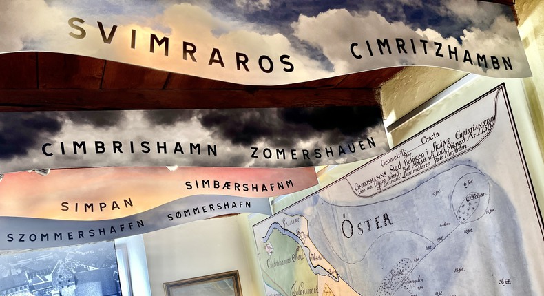 En stor karta över sydöstra Skåne sitter på en vägg, i taket hänger skyltar med äldre namn på Simrishamn.